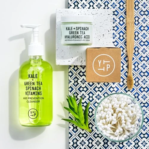 Flat lay of green tea cleanser, moisturizer, and bamboo toothbrush on patterned tile, promoting skincare and dental hygiene products.
