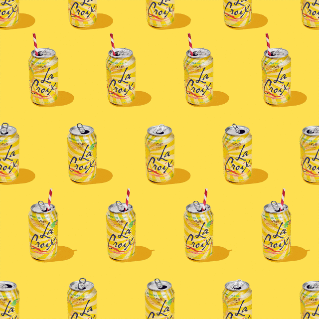 Sparkling water cans arranged in a repeating pattern on a bright yellow background, some with striped straws, under studio lighting.