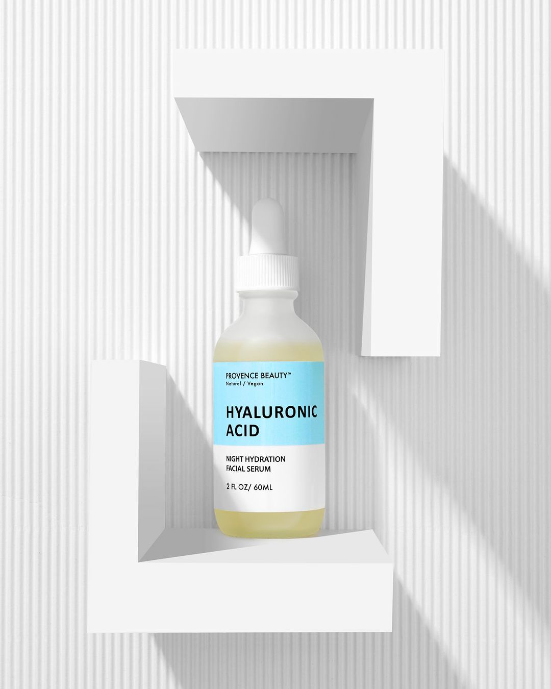 Hyaluronic acid serum in a clear bottle with a dropper, displayed on a white corner shelf against a ridged white background. 