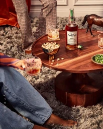 Round wooden coffee table holding a whiskey bottle, glasses with ice, small bowl of nuts, and miniature horse figurine.