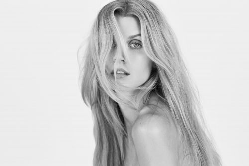 Black and white portrait of a woman with long blonde hair partially covering her face against a seamless background