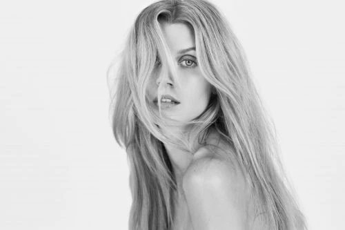 Black and white portrait of a woman with long blonde hair partially covering her face against a seamless background
