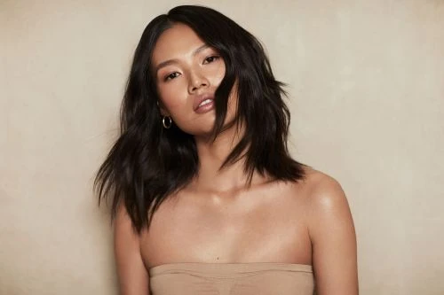Portrait of Asian woman with dark hair and tan strapless top in front of neutral background in studio lighting. Fashion and beauty shot.