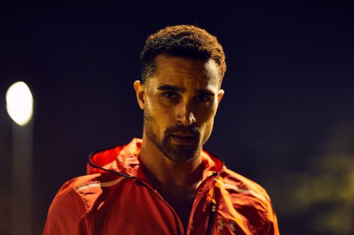 Close-up of a handsome adult man with a beard, wearing a red hooded jacket, posing outdoors at night under artificial lighting.