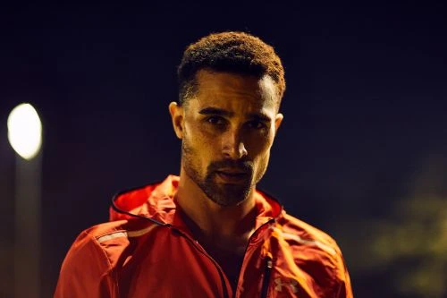 Close-up of a handsome adult man with a beard, wearing a red hooded jacket, posing outdoors at night under artificial lighting.