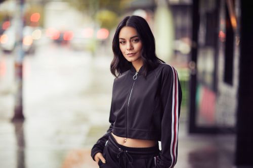 Portrait of a young adult woman with dark hair in a black tracksuit, standing on a city street with blurred urban background.