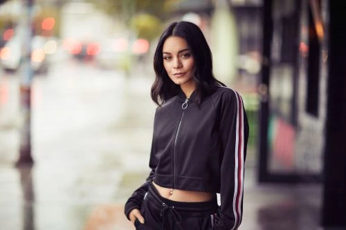 Portrait of a young adult woman with dark hair in a black tracksuit, standing on a city street with blurred urban background.