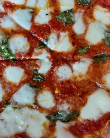Close-up of a pizza with red sauce, mozzarella cheese, and basil, showcasing its fresh ingredients and vibrant colors.