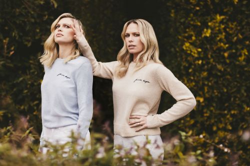 Two blonde women wearing light sweaters posing outdoors near dark foliage with Mike Rosenthal photography.