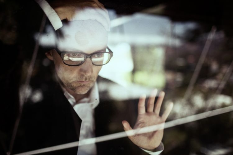 Man in glasses and suit looking through a reflective glass surface with hand raised in Los Angeles portrait