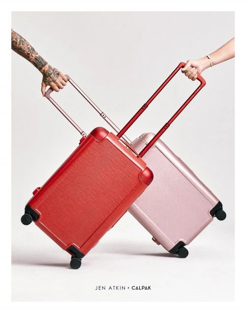 Two suitcases, one pink and one red, are positioned in the center, with a light background and hands holding the handles.