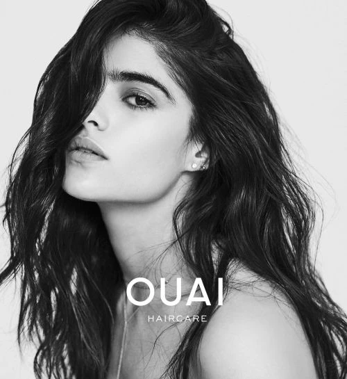 Black and white portrait of a young woman with long dark hair, showcasing a minimalist aesthetic for haircare promotion.