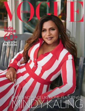 Mindy Kaling poses on a bench for the cover of Vogue India, December 2020, wearing a red and white striped dress with long brown hair.