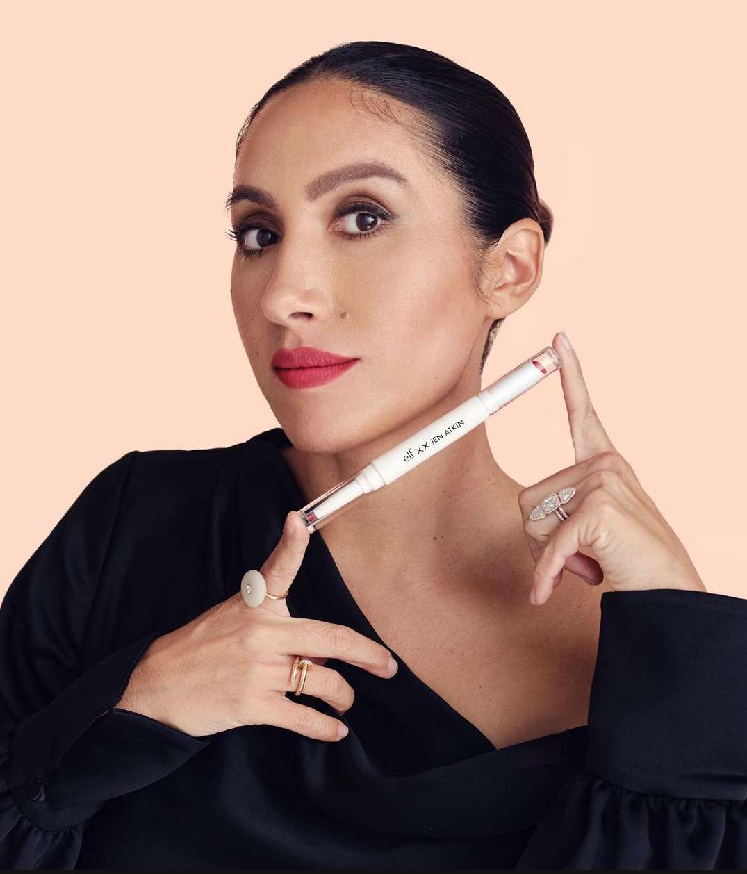 Adult female holds e.l.f. lip stain product against a peach studio backdrop, showcasing its application and design.