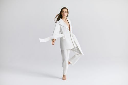 Woman in white suit posing in a studio with one leg up and fabric flowing with wind. Fashion photography for beauty and apparel.