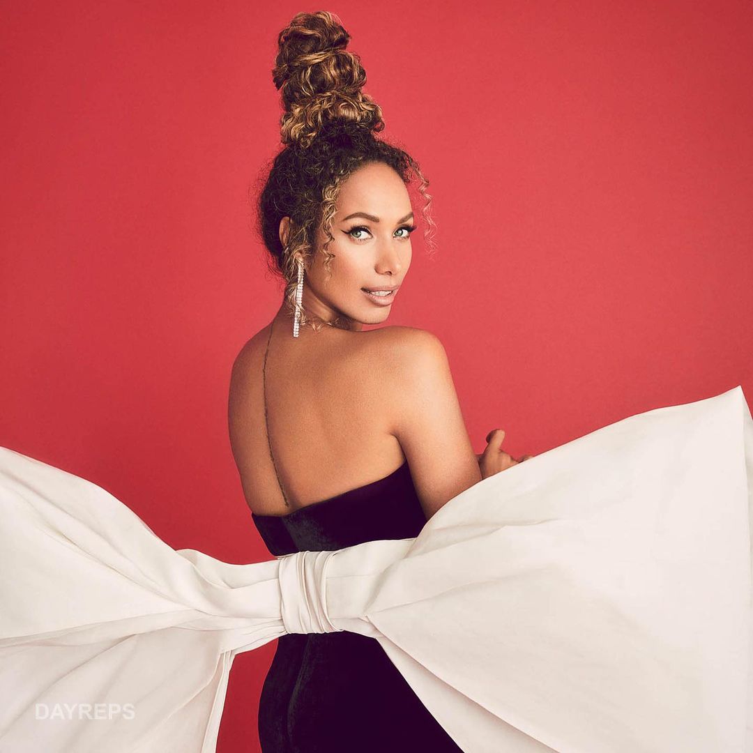Woman in dark strapless dress with large white bow posing against a red backdrop