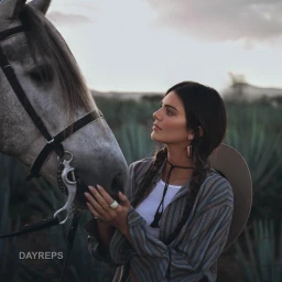 Kendall Jenner touching a white horse while wearing a striped shirt and holding a hat in an outdoor field