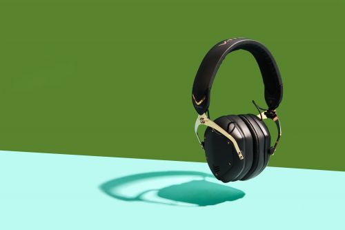 Black and gold wireless headphones are prominently displayed against a two-tone green and blue background, casting a teal shadow.
