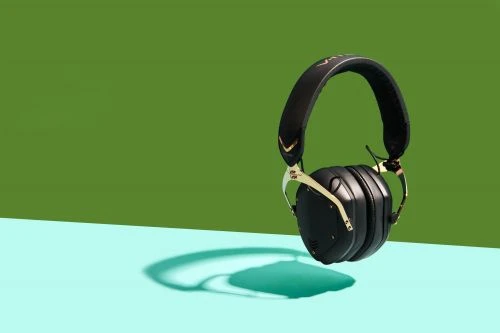 Black and gold wireless headphones are prominently displayed against a two-tone green and blue background, casting a teal shadow.