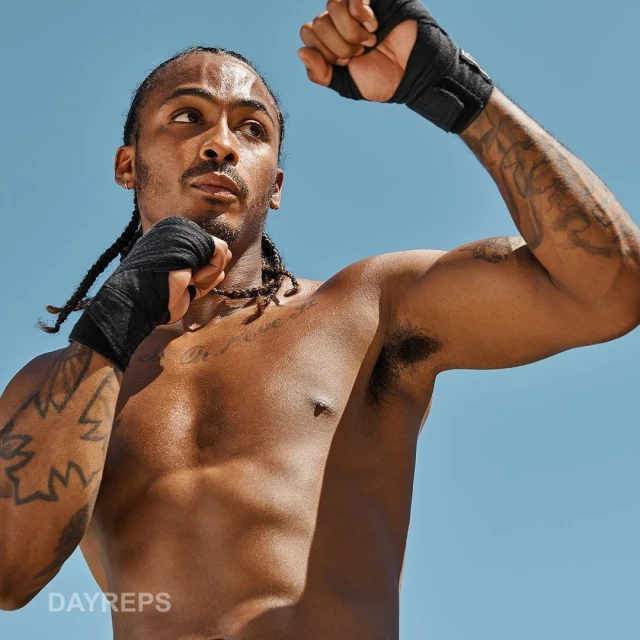 Shirtless man with boxing wraps in fighting stance against clear blue sky. Fitness workout or boxing training outdoors in sunshine.