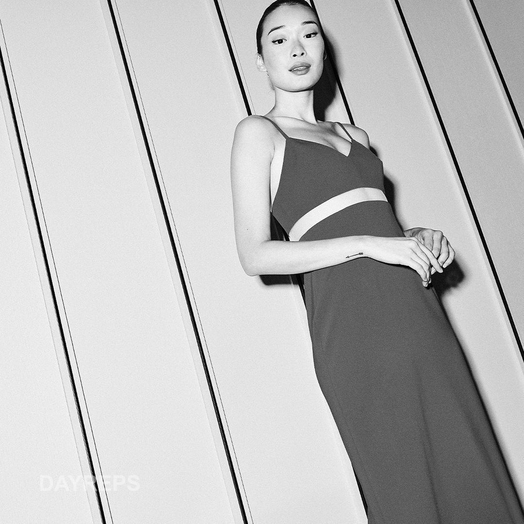 Portrait of a young woman in a stylish cut-out dress against a white wall, showcasing fashion and minimalist aesthetic.