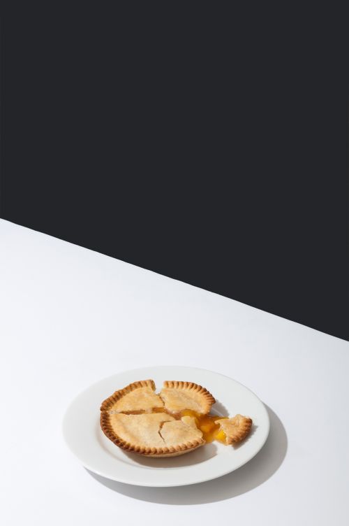 Eye-level studio shot of a peach pie with a slice missing on a white plate against a dark backdrop, showcasing minimal food photography.