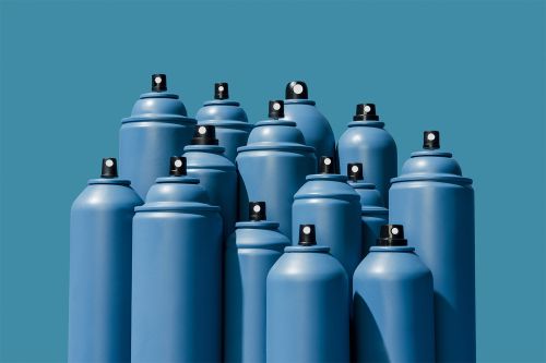 Many blue spray paint cans are grouped together on a blue background in a studio, creating a visually striking monochrome arrangement.