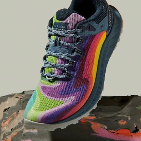 Merrell trail running shoe featuring a vibrant rainbow color pattern on a textured grey surface. Close-up product shot.