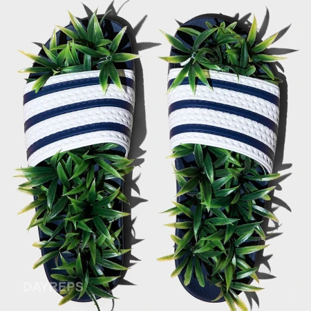 Pair of navy and white striped sandals with green leafy plants sprouting from them, set on a neutral-toned surface, studio shot.