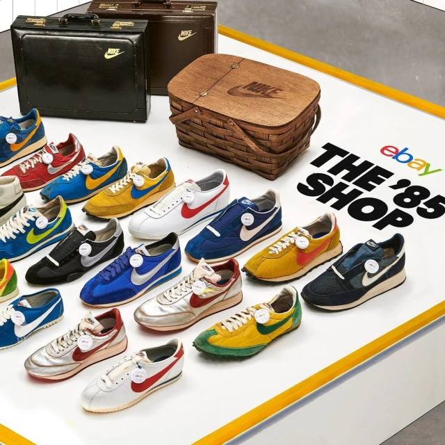 A display of multiple pairs of vintage Nike sneakers, briefcases, and a wooden picnic basket against a white and yellow background.