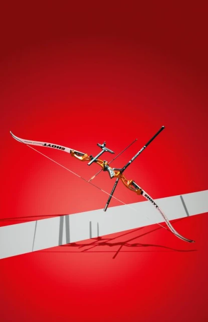 A modern recurve bow in a studio setting, angled with metallic and white accents, set against a vibrant red background with a white stripe.