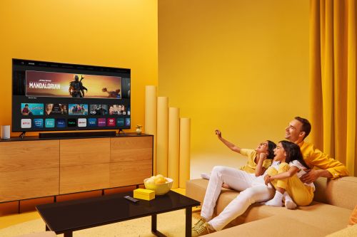 Family of three relaxing together while watching TV in a yellow living room with a modern media console and minimalist decor.