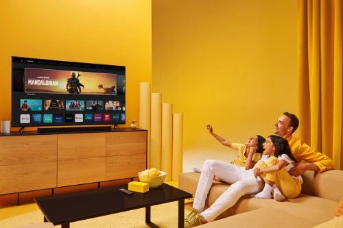 Family of three relaxing together while watching TV in a yellow living room with a modern media console and minimalist decor.