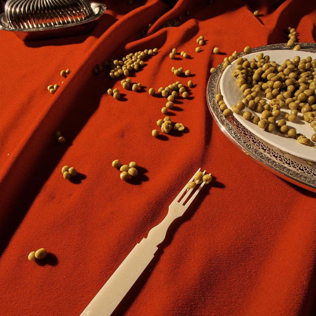 Overhead shot of a plate and loose peas on a red cloth, with silverware and a fork scattered around, creating an abstract food scene.
