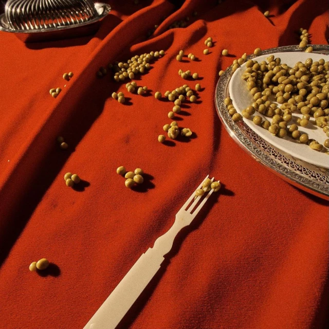 Overhead shot of a plate and loose peas on a red cloth, with silverware and a fork scattered around, creating an abstract food scene.