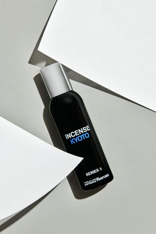 A black perfume bottle with a silver cap stands out against white geometric shapes and a soft grey background in a beauty still life.
