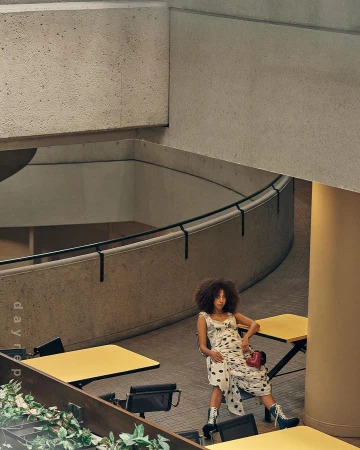 Woman in patterned dress seated at yellow table in concrete architectural atrium by Molly Cranna