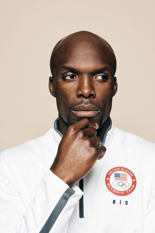 Portrait of an African American male wearing a white Olympic team jacket, looking thoughtfully to the side against a neutral backdrop.
