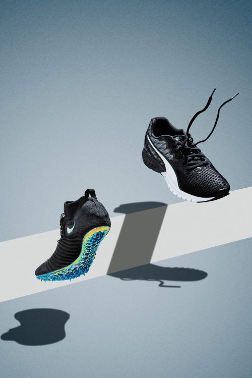 Two athletic shoes, one black and one black with white sole, are floating on a grey surface with shadows, suggesting movement and lightness.