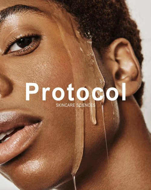 Close-up studio shot of an adult woman with dark hair and glowing skin, water cascading down the side of her face. White background.