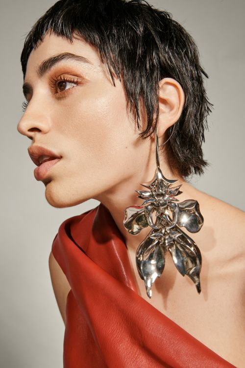 Close-up portrait of a woman wearing a large silver statement earring and red leather top against a neutral background
