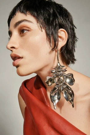Close-up portrait of a woman wearing a large silver statement earring and red leather top against a neutral background