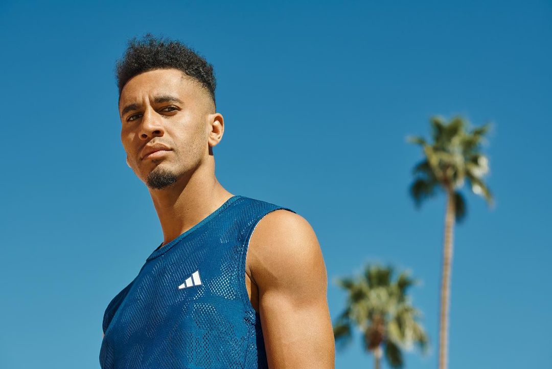 Portrait of an adult male wearing a blue Adidas tank top with palm trees and a blue sky in the background on a sunny day.