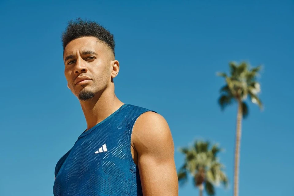 Portrait of an adult male wearing a blue Adidas tank top with palm trees and a blue sky in the background on a sunny day.