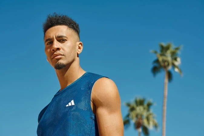 Portrait of an adult male wearing a blue Adidas tank top with palm trees and a blue sky in the background on a sunny day.