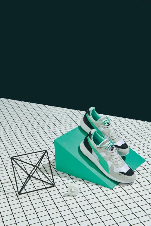 Pair of Puma athletic shoes displayed on a green geometric block and white grid surface against a dark green backdrop. Product shot.