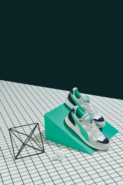 Pair of Puma athletic shoes displayed on a green geometric block and white grid surface against a dark green backdrop. Product shot.
