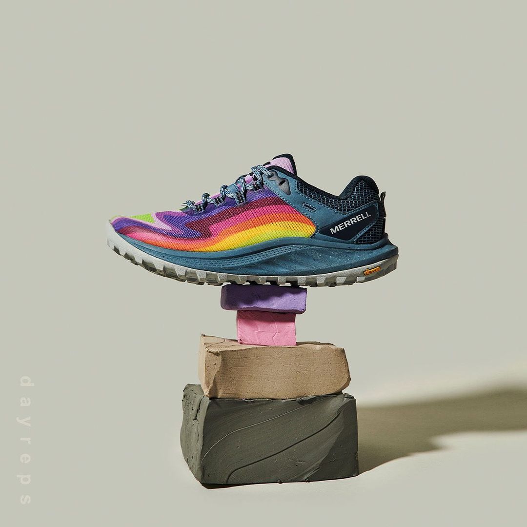 Merrell trail running shoe floats in a studio shot, balanced atop stacked cubes, showcasing its colorful design and rugged sole.