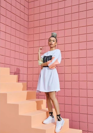 Woman in white dress and sneakers standing on pastel stairs against a pink tiled wall