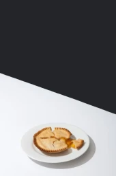 A sliced fruit pie on a white plate resting on a white tabletop against a dark grey background, photographed by Molly Cranna.